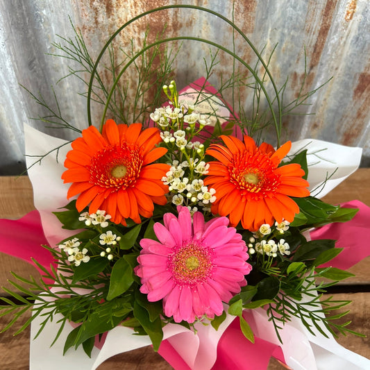 Bouquet of flowers with orange, pink, and white flowers on a wooden surface.