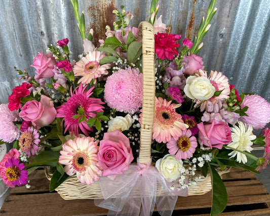 Bouquet of pink and white flowers in a woven basket against a rustic metal wall.