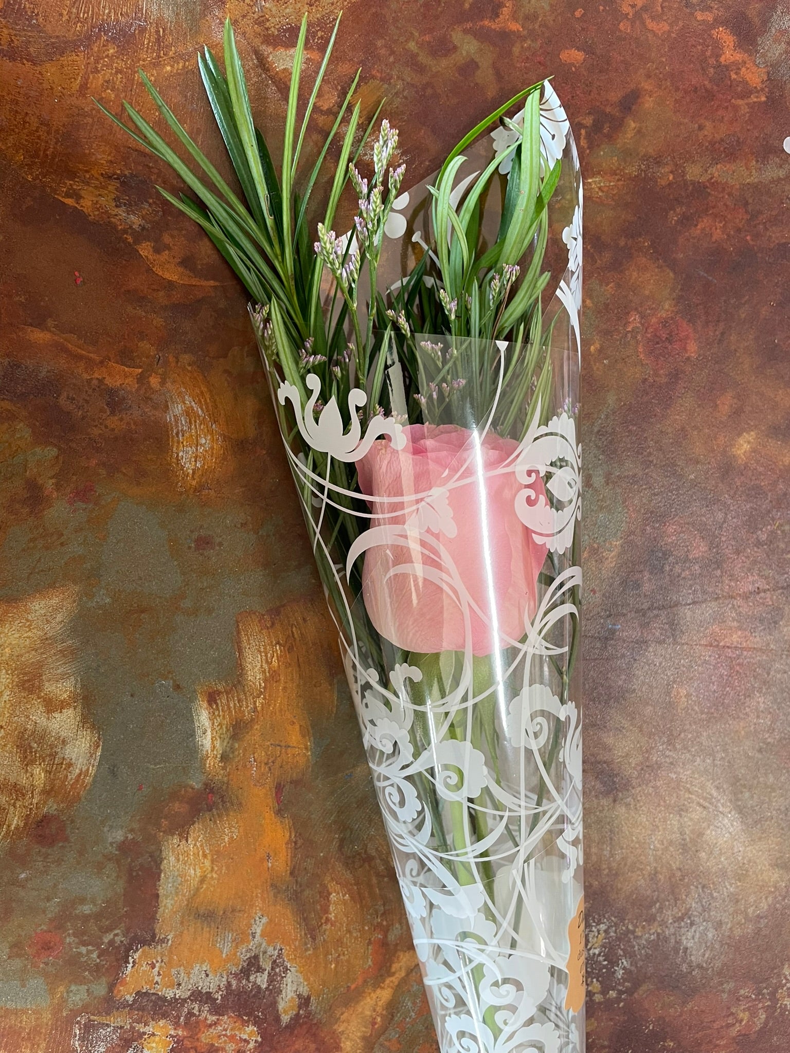 Bouquet of pink roses and greenery in clear wrap on a textured brown background