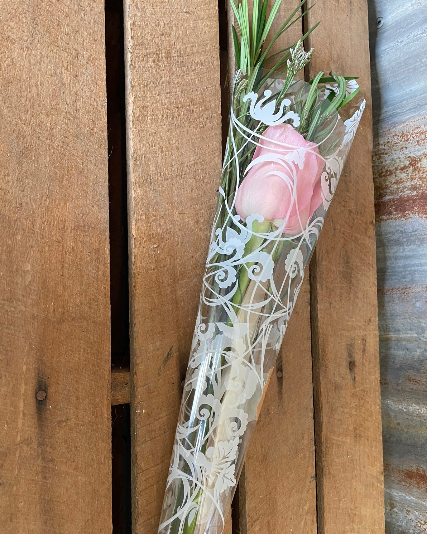 Bouquet of pink roses wrapped in cellophane against a wooden background