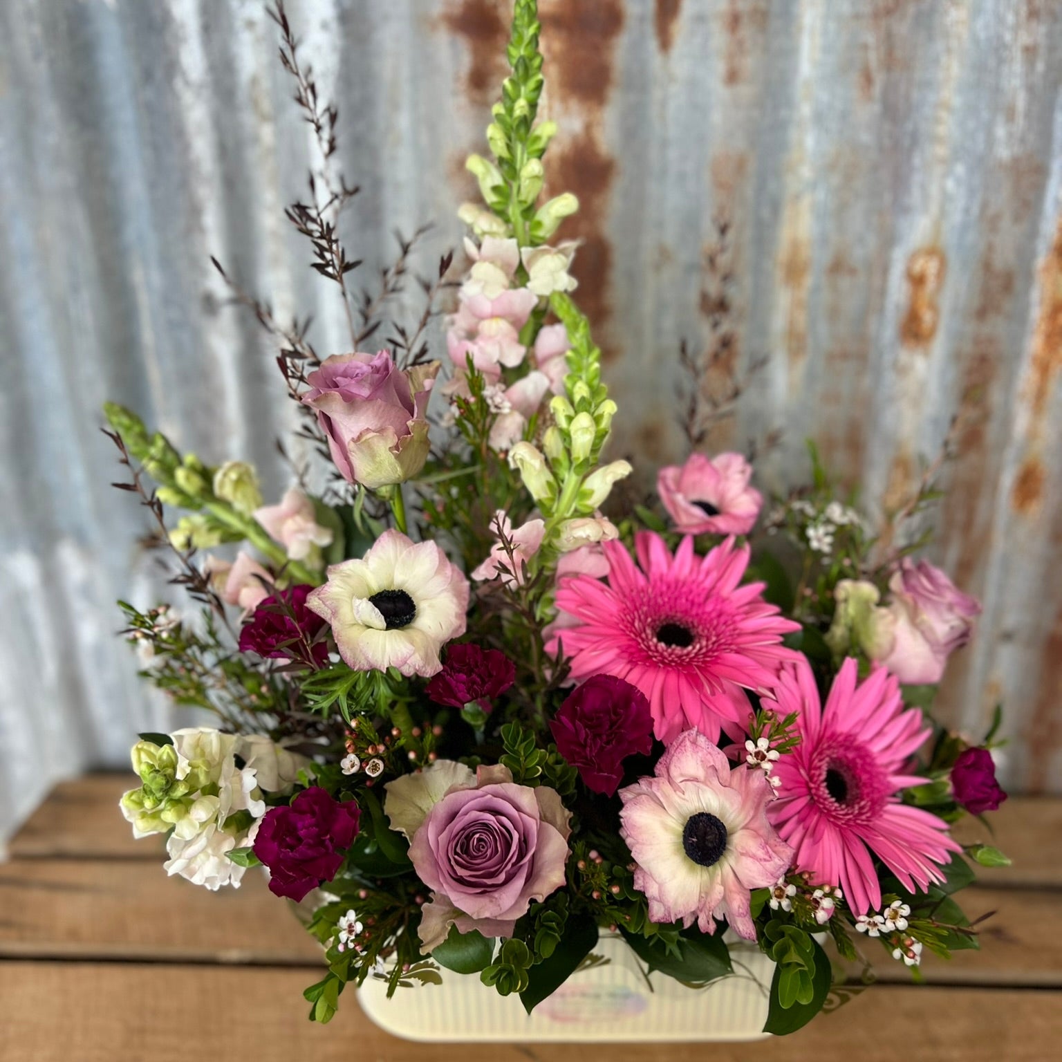 Floral arrangement with pink, white, and purple flowers on a wooden surface with a rustic metal background.