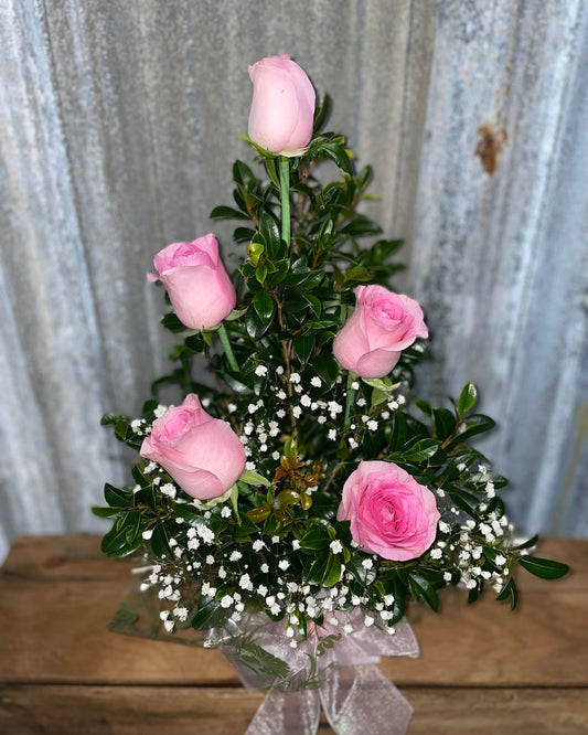 arrangement of pink roses with greenery on a wooden surface and textured white background