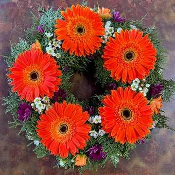 Floral wreath with orange flowers and greenery on a textured brown background